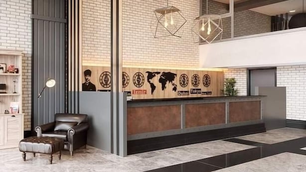 A modern reception area with a brick wall, a leather chair, and a reception desk featuring a world map and city names. - Ramada by Wyndham Tire (Tire)
