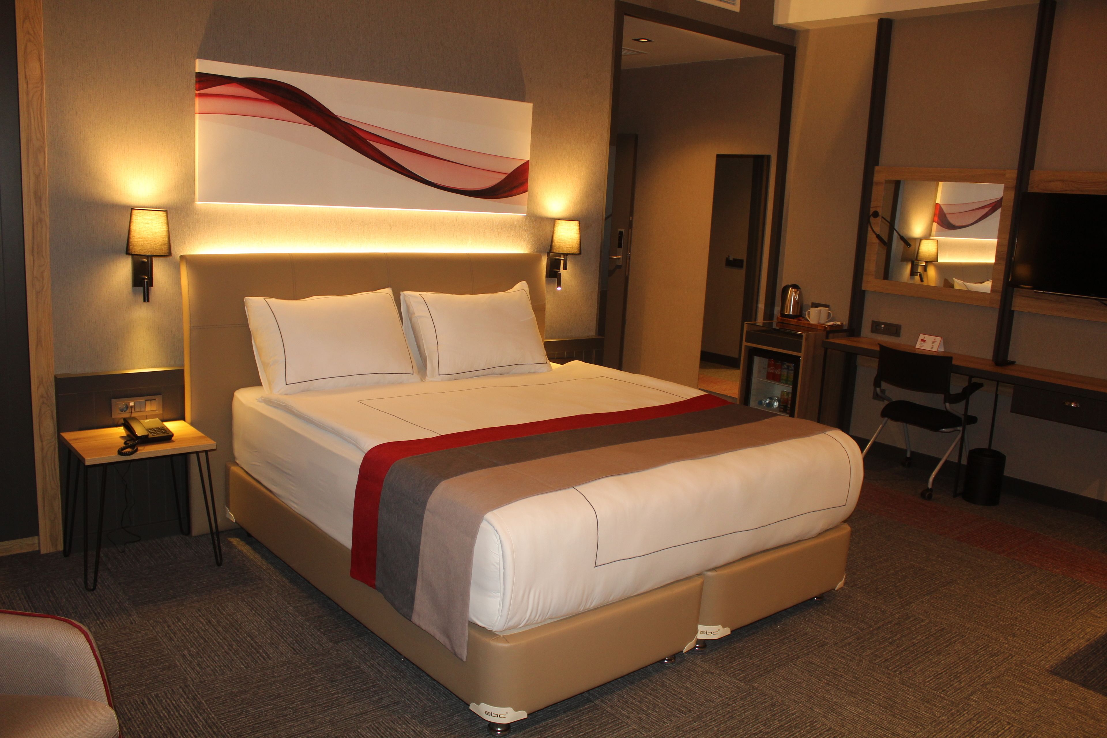 Una habitación de hotel con una cama grande, mesitas de noche, un escritorio, una silla y un televisor.