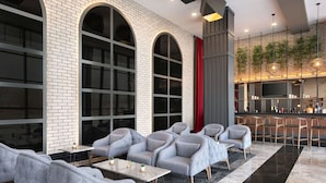 A modern lounge area with grey upholstered seating, a bar with stools, and a large TV screen. - Ramada by Wyndham Tire (Tire)