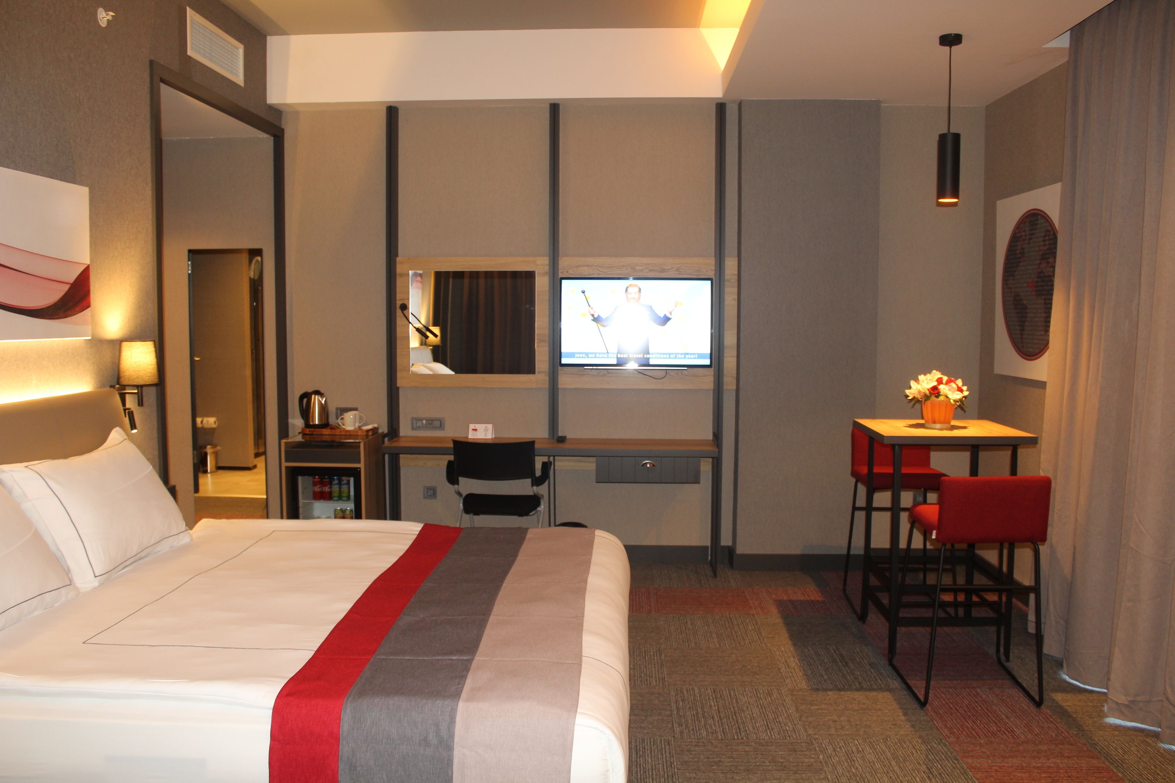 A hotel room with a bed, a desk, a chair, a television, and a small table with a vase.