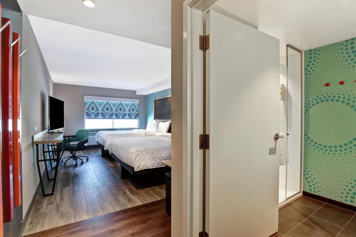 A modern hotel room with a bed, desk, chair, and a large window.
