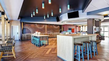 Et moderne barområde med en gulv i fiskebensmønster af træ, en midterstillet bar og blå barstole.