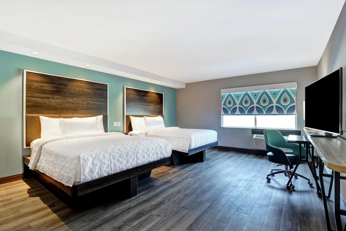 A hotel room with two beds, a desk, and a large window.