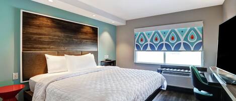 A modern hotel room with a large bed, a desk, and a window with a decorative view.