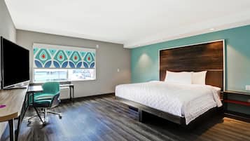 A modern hotel room with a large bed, a desk with a chair, a TV, and a window with a city view.