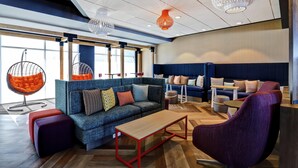 A modern lounge area with a blue sofa, purple armchair, and orange hanging chairs. - TRU BY Hilton Edmonton Windermere (Edmonton)