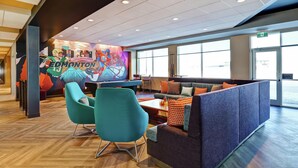 A modern lounge area with seating, a mural, and large windows. - TRU BY Hilton Edmonton Windermere (Edmonton)