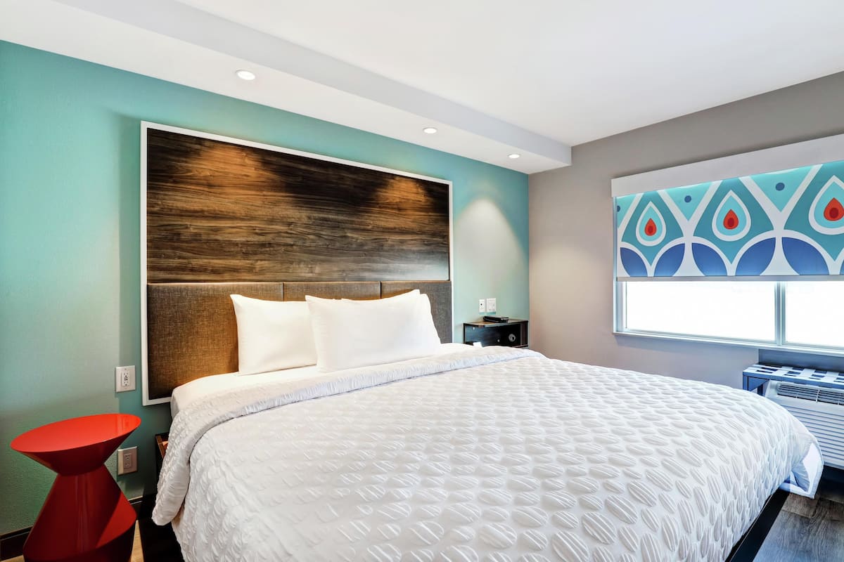 A modern hotel room with a large bed, a red accent table, and a decorative wall panel.