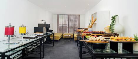 Une chambre d’hôtel moderne dotée d’un coin repas avec un buffet proposant divers plats, d’un canapé et d’une télévision.