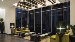Una sala de estar moderna con un sofá amarillo, otomanas negras y un ventanal con vistas a la ciudad.