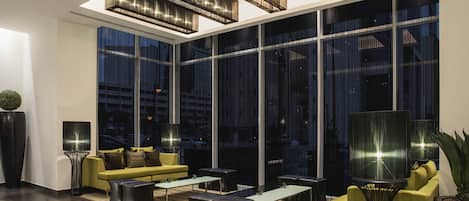 A modern living room with a yellow sofa, black ottomans, and a large window with a city view.