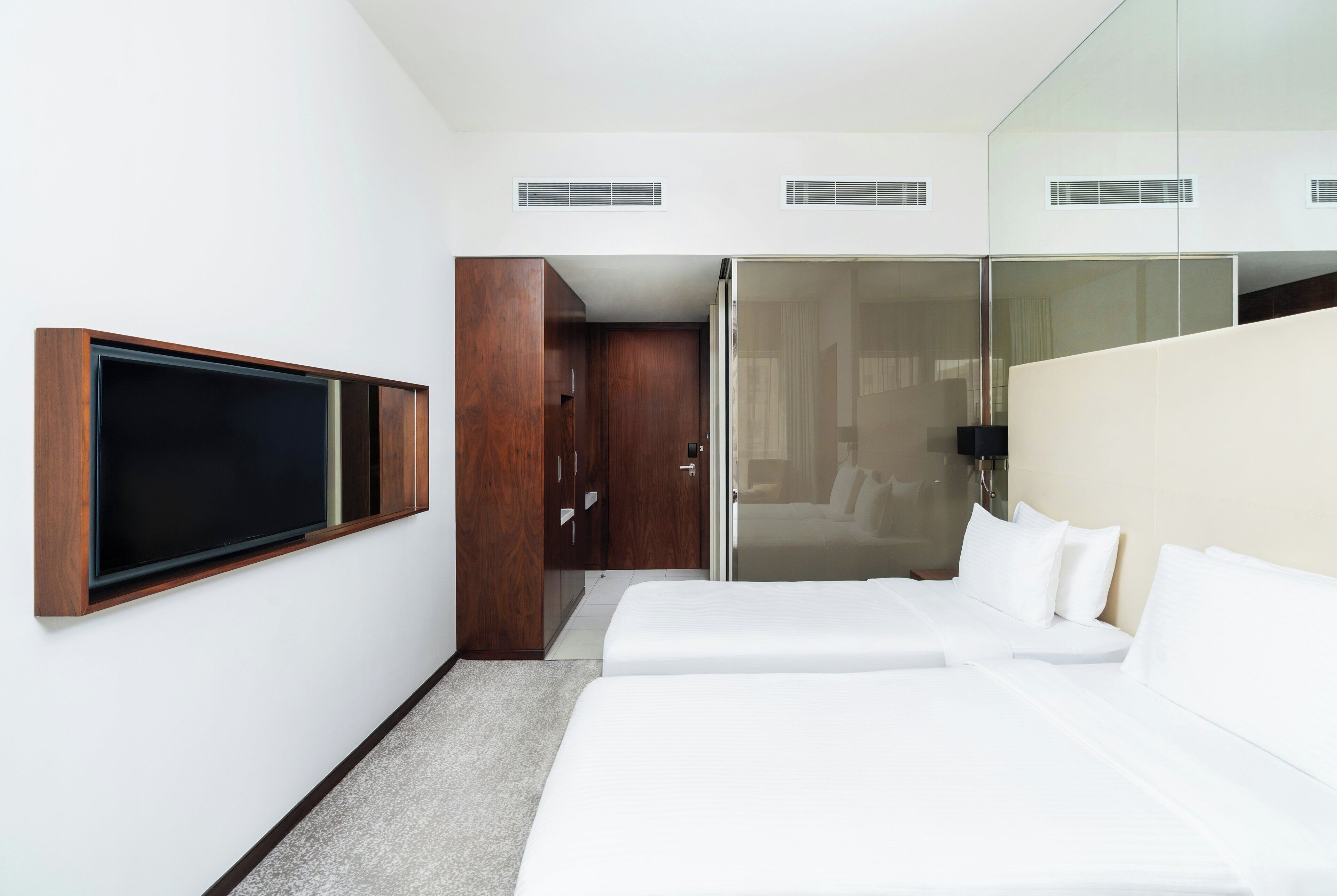 Habitación de hotel con televisor montado en la pared, armario, cama y separador de vidrio.