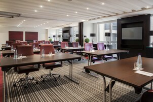 A modern conference room with multiple tables and chairs, equipped with water bottles and glasses, and a large screen displaying a graph.