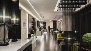 Un moderno vestíbulo de hotel con un mostrador de recepción alargado, decoración en blanco y negro y una escalera que conduce a pisos superiores.