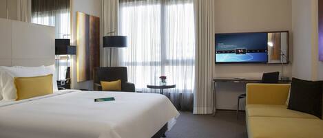 A hotel room with a large bed, a desk, a chair, a sofa, and a TV.
