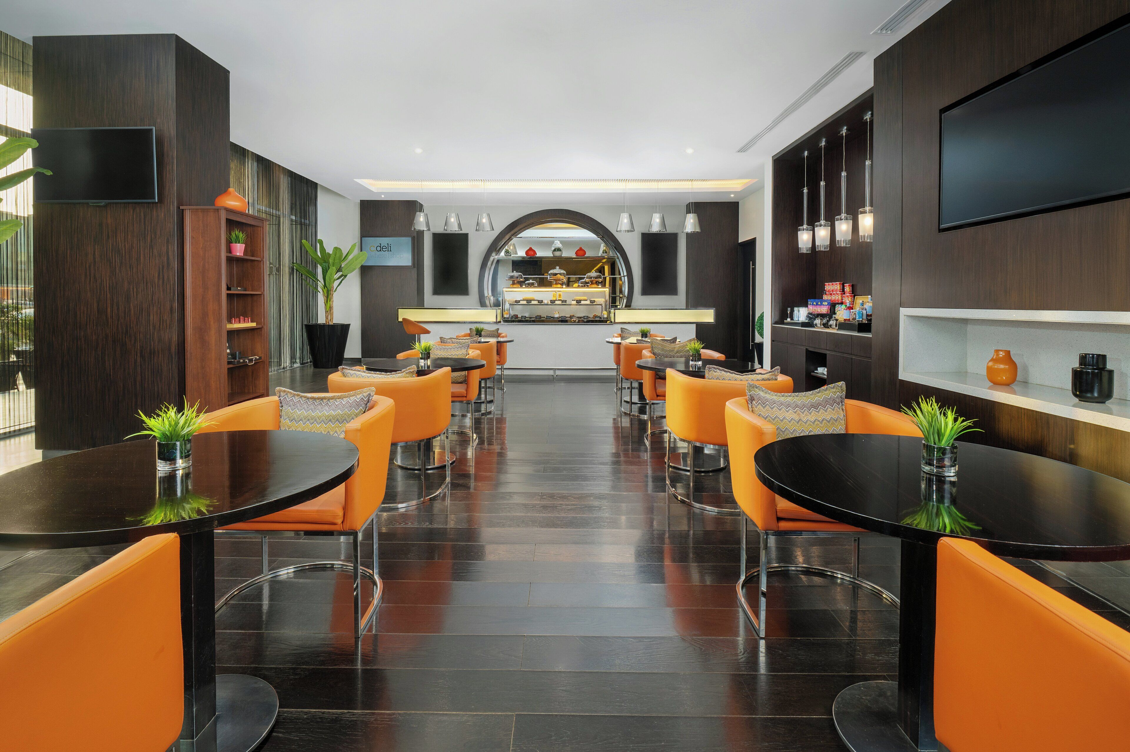 Eine moderne Hotelhalle mit Barbereich, Sitzgelegenheiten und einem großen Flachbildfernseher an der Wand.