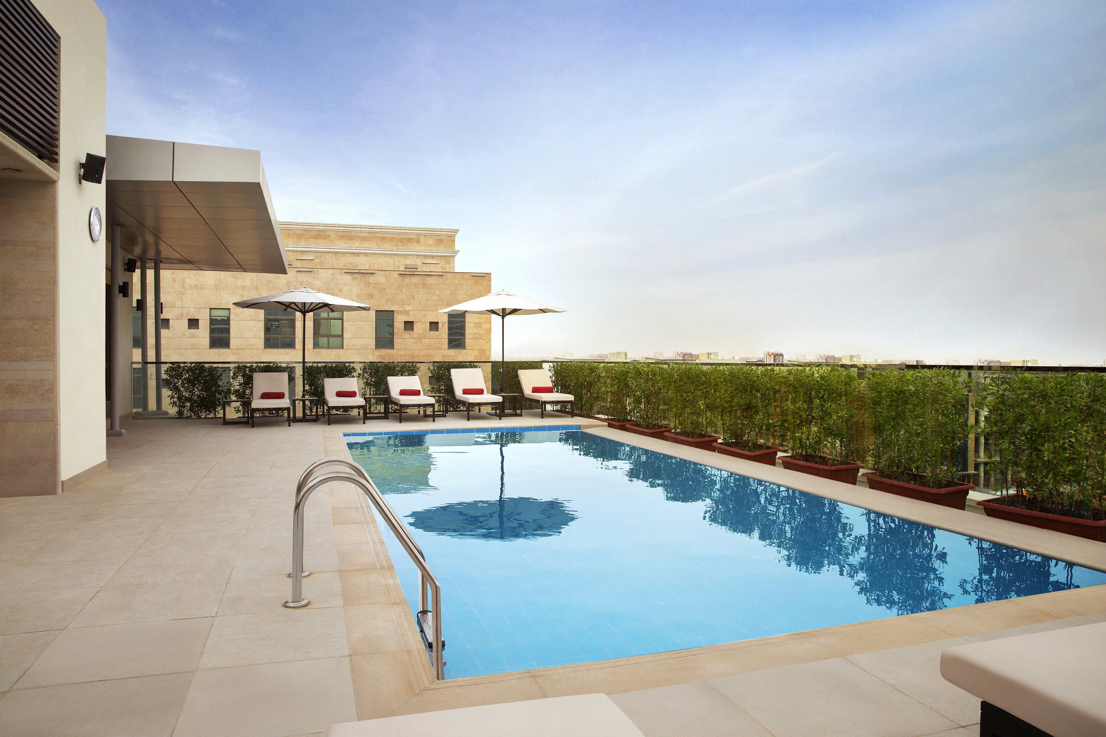 A swimming pool with lounge chairs and umbrellas, surrounded by potted plants and a building in the background.