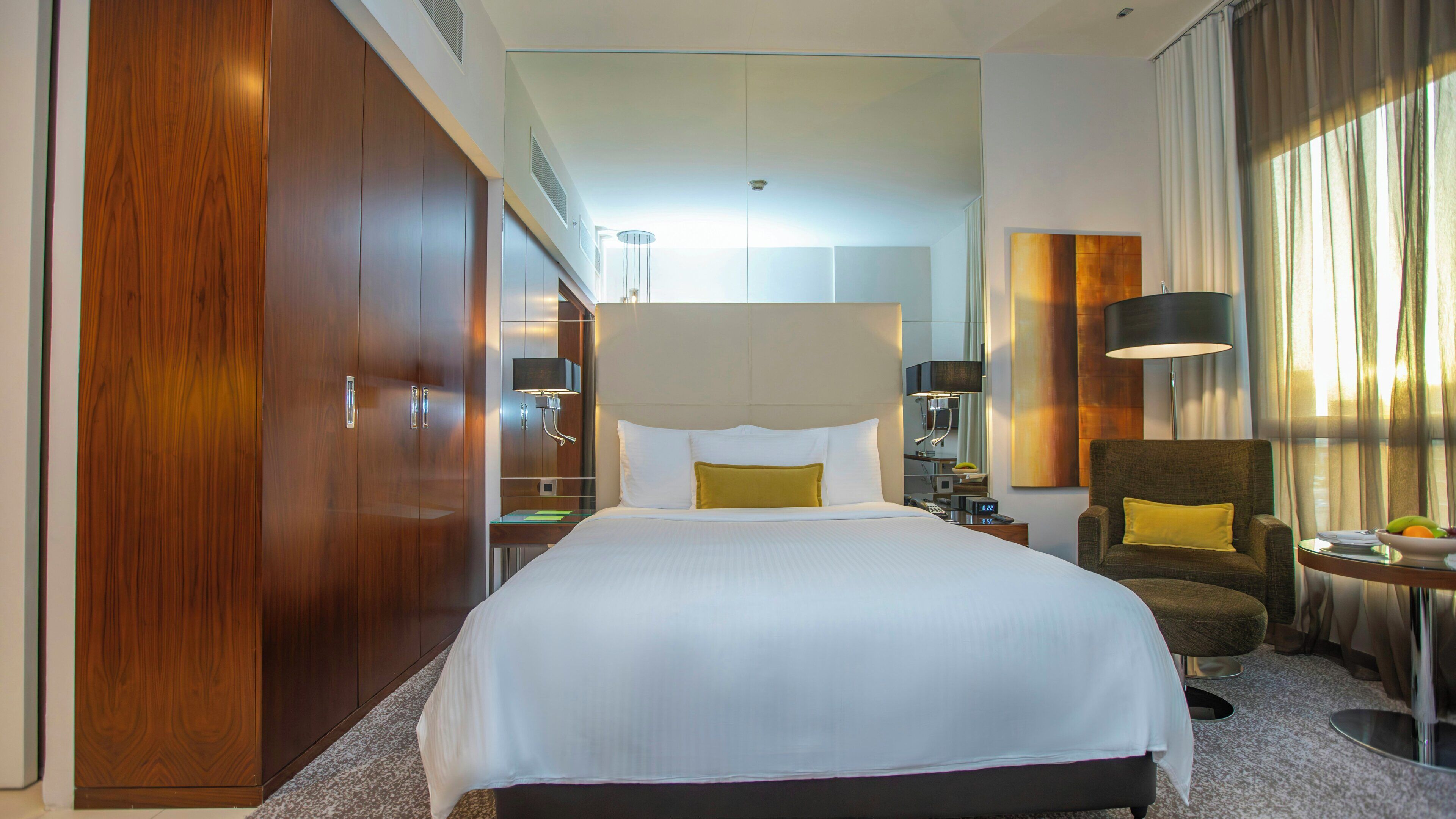 Habitación de hotel con una cama grande, un armario, un escritorio, una silla y una lámpara.
