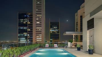 Una piscina en la azotea con vistas a un paisaje urbano, edificios modernos y plantas en macetas.