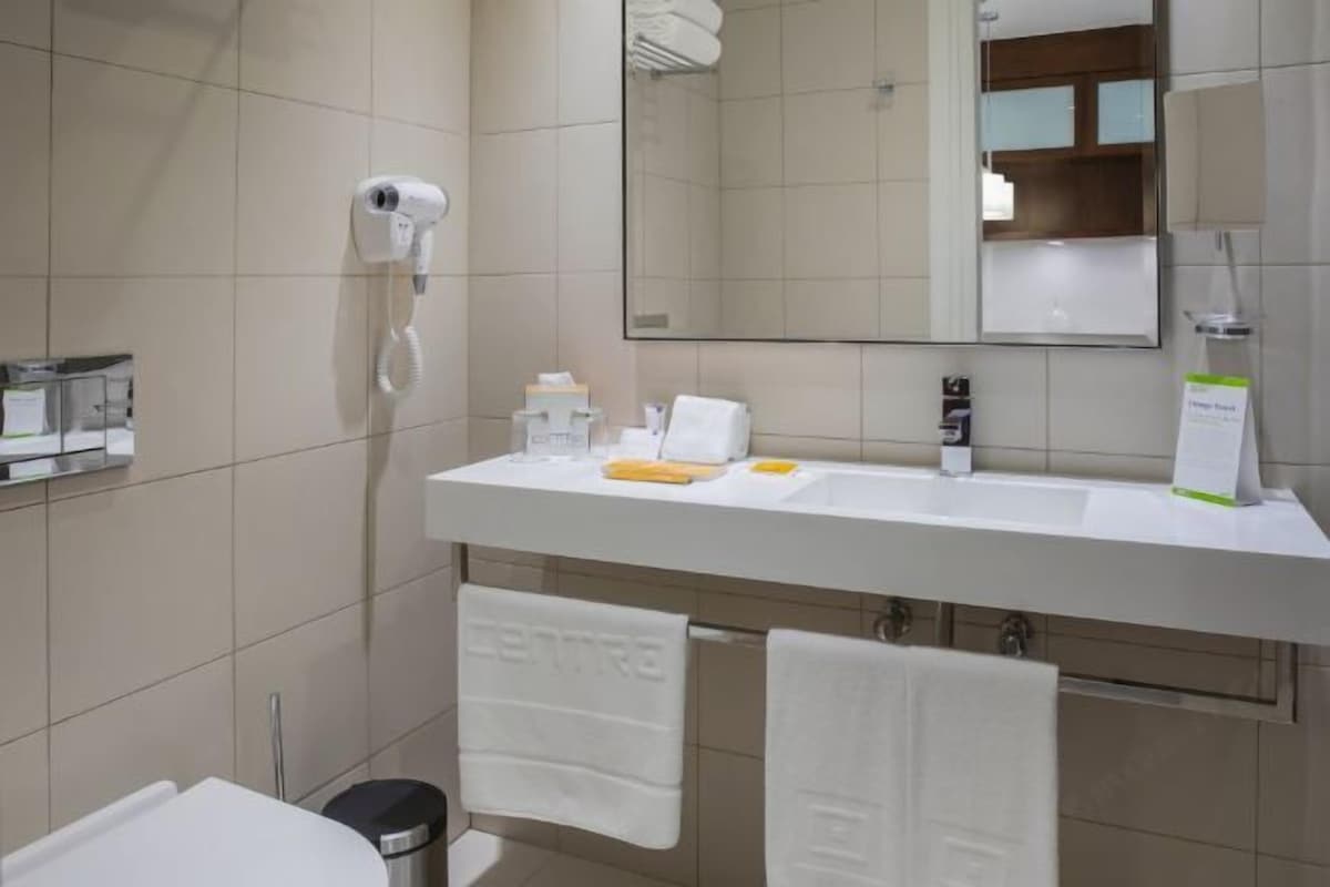 Une salle de bain moderne avec un lavabo blanc, un miroir, un sèche-cheveux et deux serviettes.