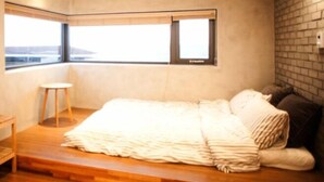 A bedroom with a bed, a small table, a lamp, and a window with a view. - Sinchon Blues (Jeju City)