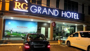 The exterior of the RG Grand Hotel with a signboard, a parked black car, and a white car in front. - RG Grand Hotel (Batu Pahat)