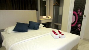 A neatly made bed with white linens and two pillows, a small bedside table with a lamp, and a door with a decorative mirror and a circular design. - RG Grand Hotel (Batu Pahat)