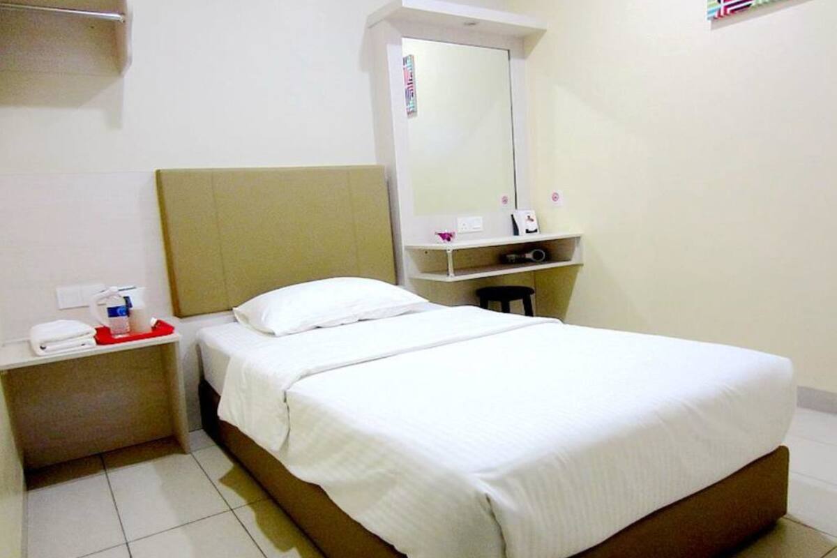 A hotel room with a single bed, a nightstand, a mirror, and a small shelf with toiletries.