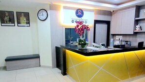 A hotel reception area with a yellow reception desk, a clock, framed pictures on the wall, and a sign above the desk. - RG Grand Hotel (Batu Pahat)