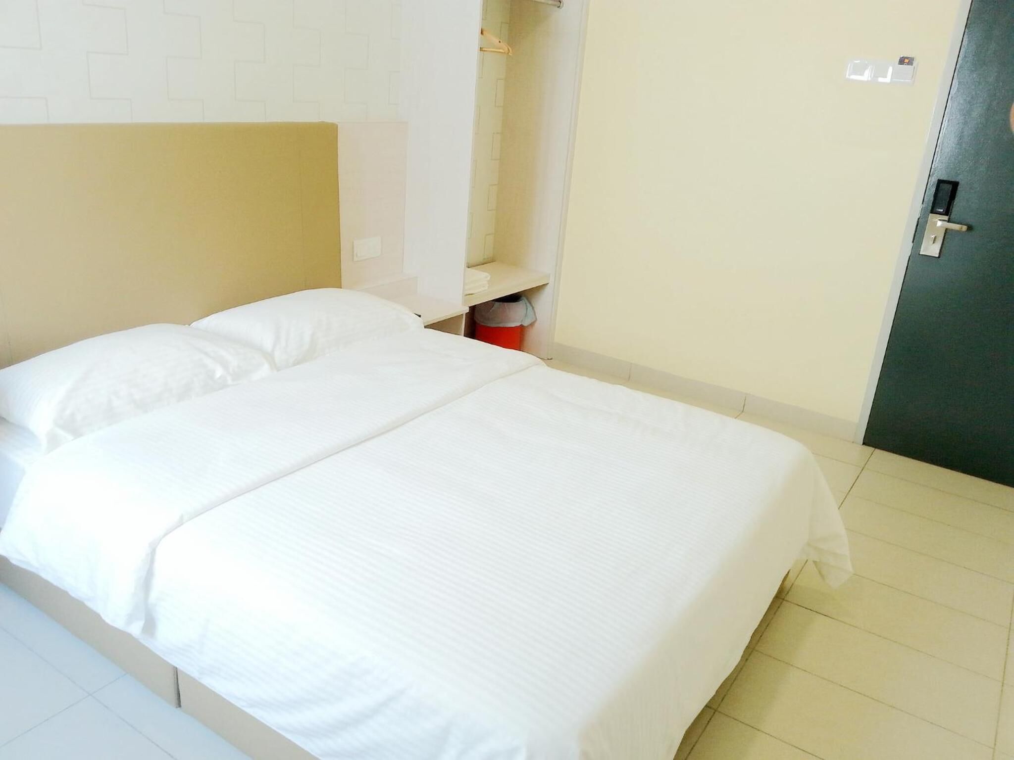 A single bed with white bedding in a room with a tiled floor and a plain wall.