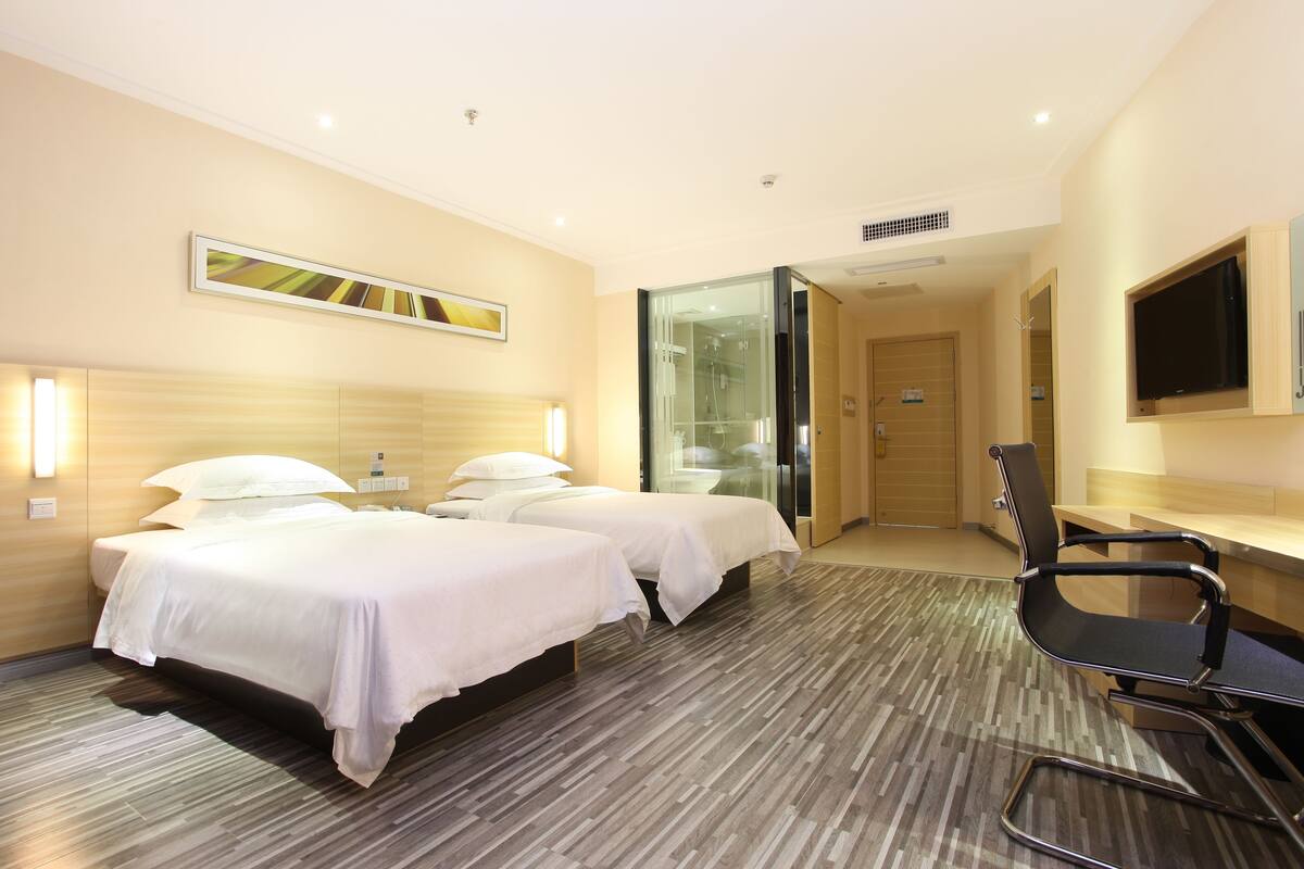 A hotel room with two beds, a desk, a chair, a TV, and a bathroom.