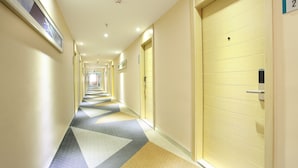 Ein Hotelkorridor mit einem gemusterten Teppich, rechts Türen und links ein gerahmtes Bild.