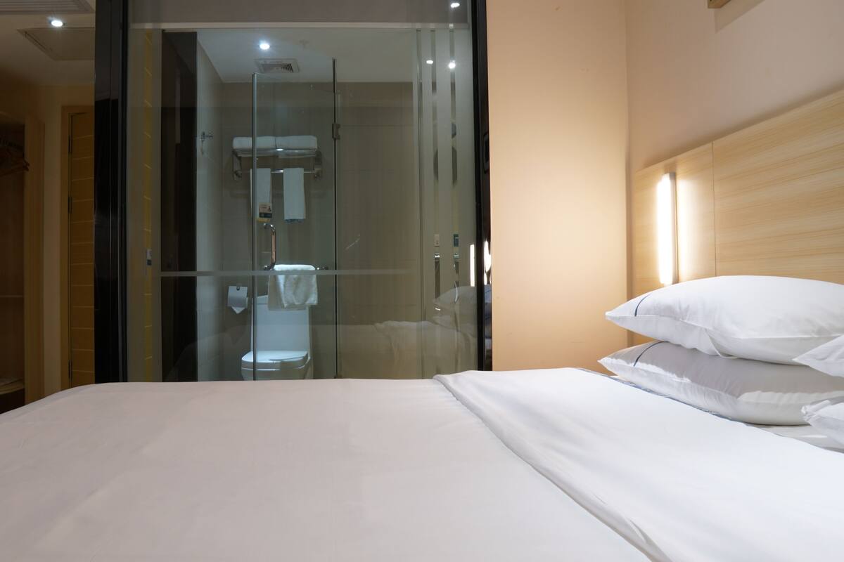 A hotel room with a bed, a glass-enclosed shower, and a wooden wardrobe.
