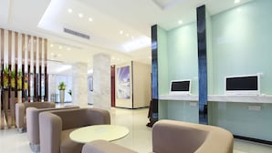 Eine moderne Lobby mit Sofas, einem runden Tisch und zwei Monitoren an einer Theke.