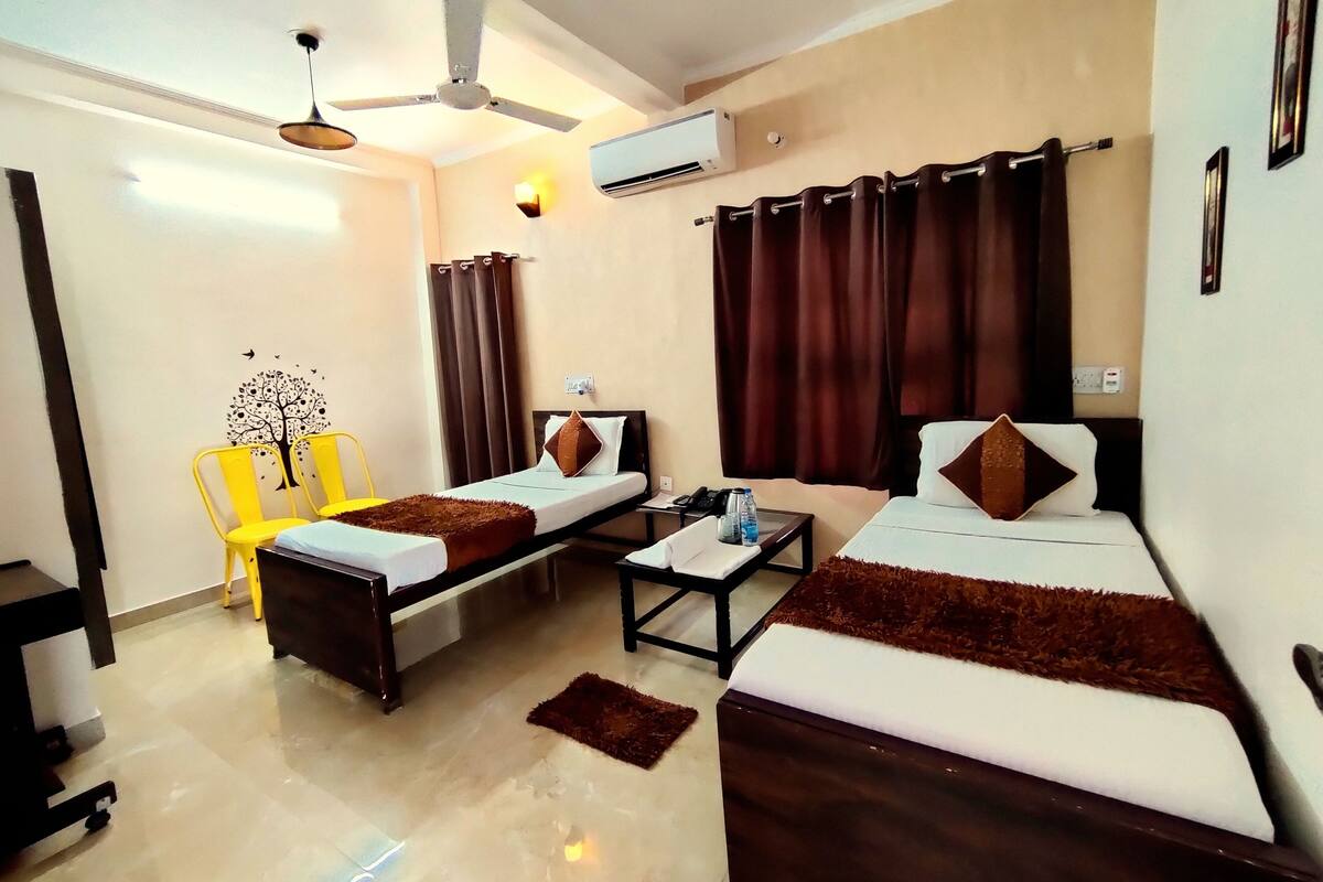 A hotel room with two beds, a desk, a chair, an air conditioning unit, and a ceiling fan.