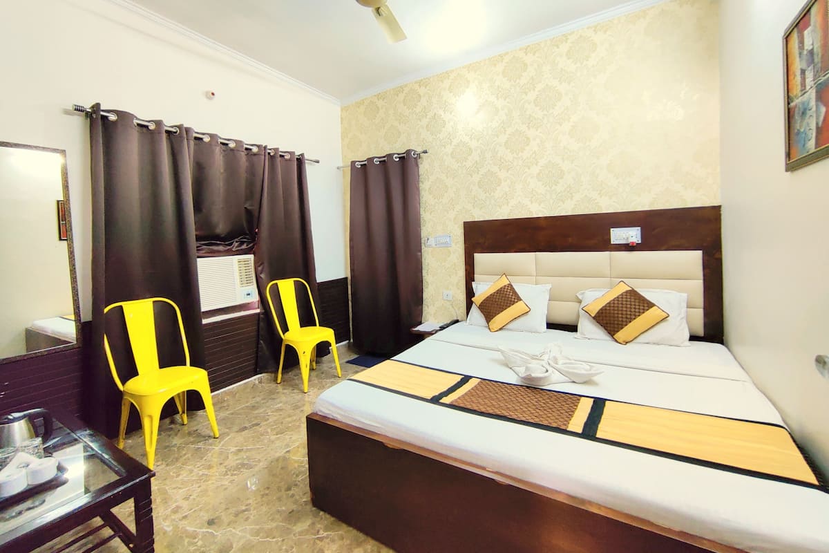 A hotel room with a bed, two chairs, a table, a ceiling fan, and a window with curtains.
