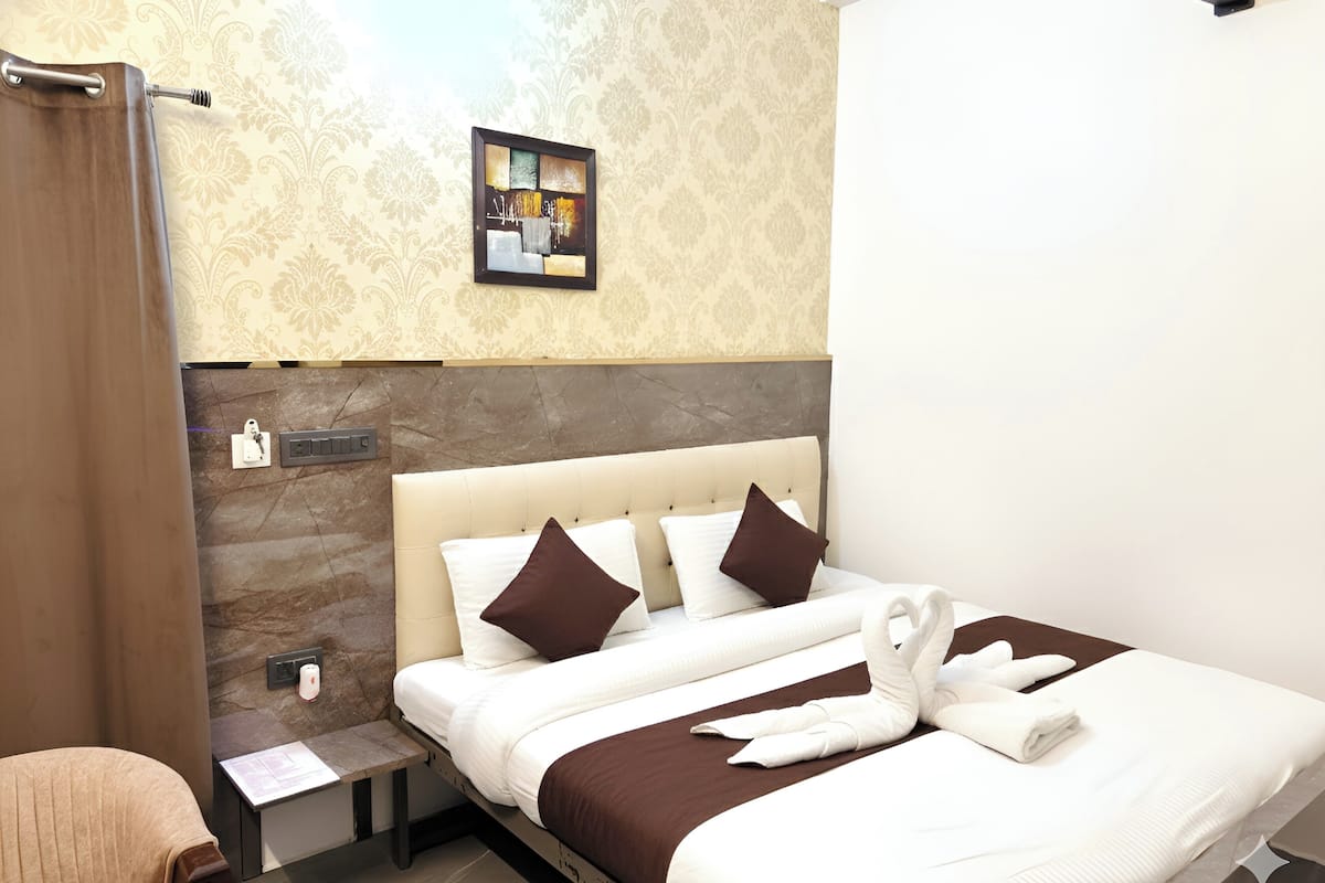A hotel room with a bed, a nightstand, a towel rack, and a wall-mounted artwork.