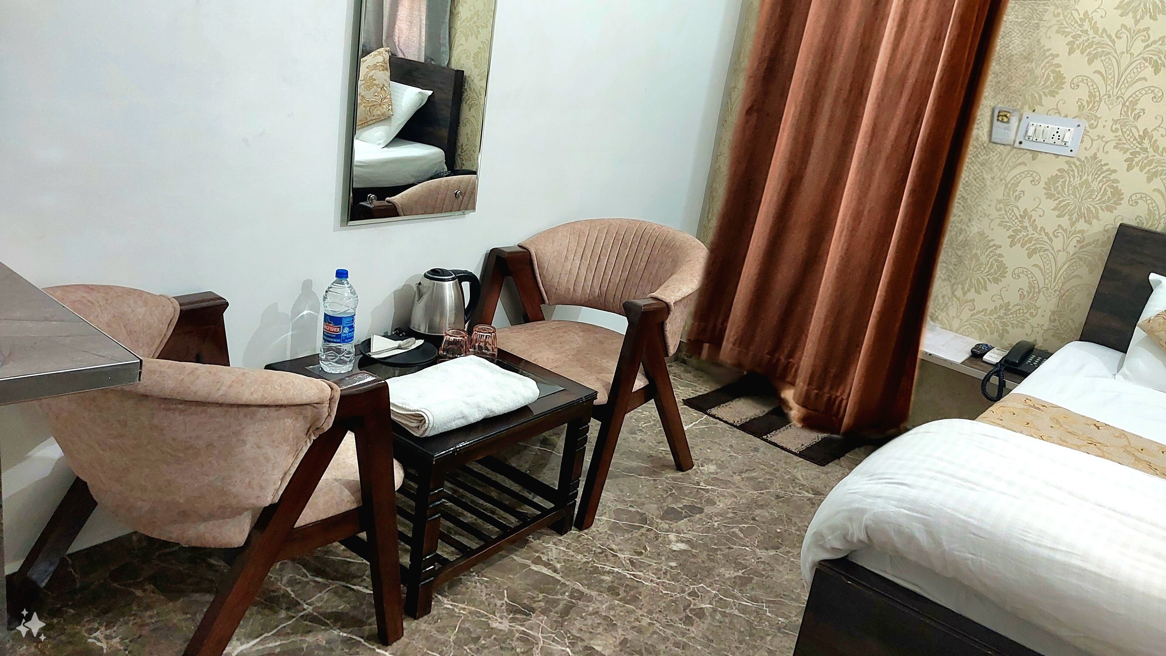 Habitació d'hotel amb llit, escriptori amb cadira, taula amb ampolla d'aigua, tetera i telèfon.