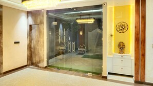 A modern interior with a glass door entrance, a chandelier, and a small statue on a wooden cabinet. - Krishna Residency - A Boutique Hotel (Bareilly)