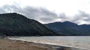 Una playa con barcos y una montaña boscosa al fondo.