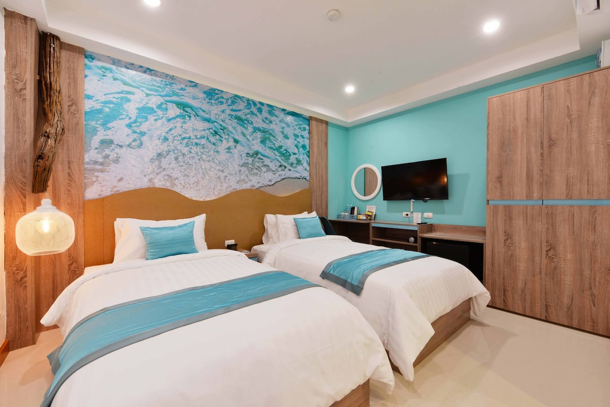 A hotel room with two beds, a large mural, a TV, and wooden furniture.