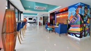 Un moderno vestíbulo de hotel con una larga recepción, una zona de estar azul y un mural colorido.