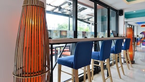 Zona de bar con sillas azules, una mesa de madera larga y lámparas anaranjadas altas.