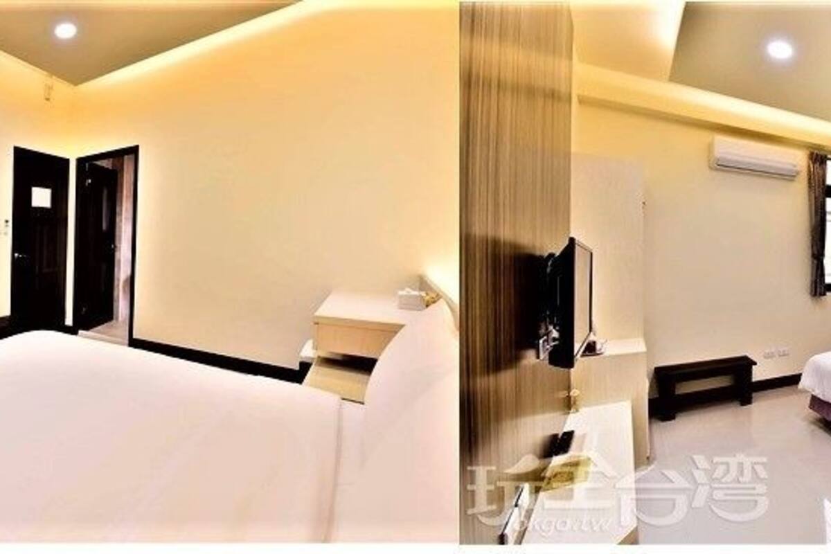 A modern hotel room with a large bed, a TV mounted on the wall, a bedside table, and a window with curtains.