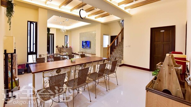 Un vaste espace dédié à la salle à manger, avec une longue table en bois et des chaises en osier, un lustre et un téléviseur fixé au mur.