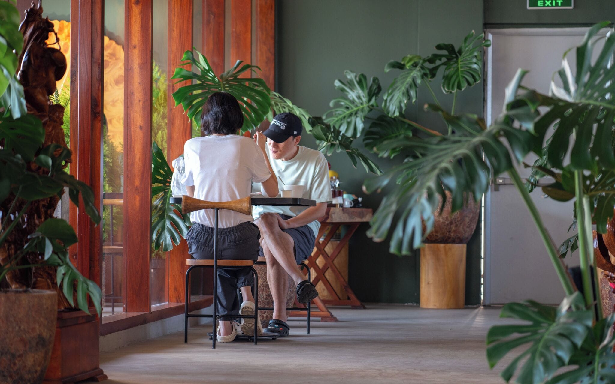A cafe with wooden furniture, large green plants, and a rustic interior.