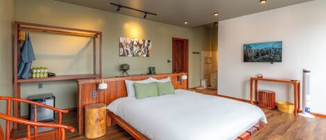 A modern bedroom with a wooden bed, a wooden desk, a chair, and a small table with a lamp.