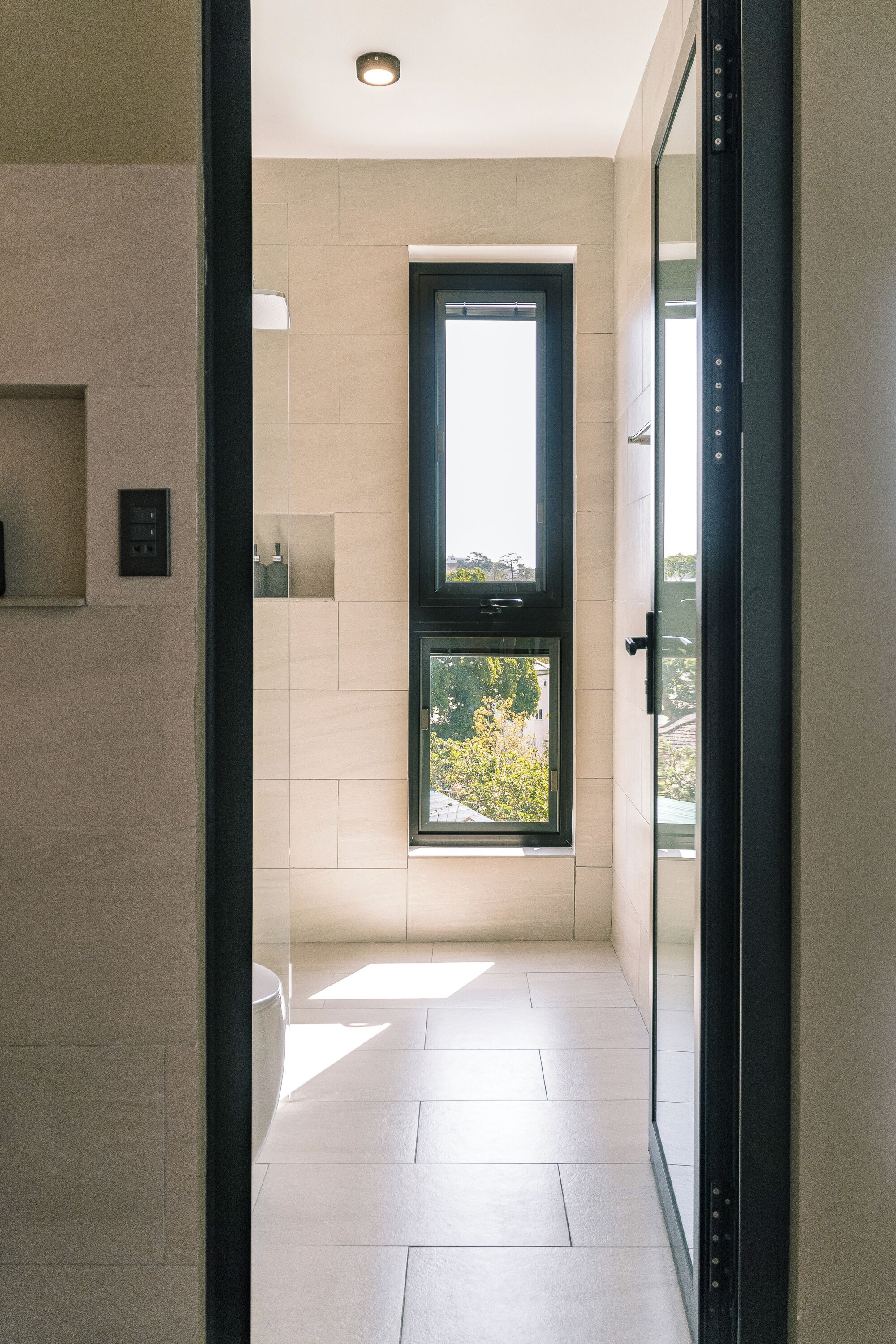 A modern bathroom with a large window, a toilet, and a shower area.