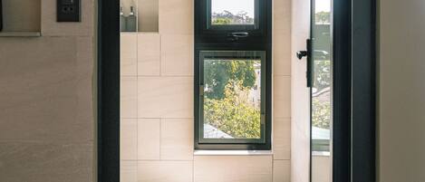 A modern bathroom with a large window, a toilet, and a shower area.