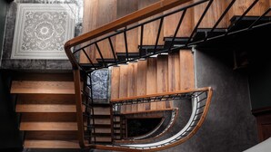 Una escalera de caracol con escalones de madera y barandillas de metal, que lleva a un rellano con suelo estampado.